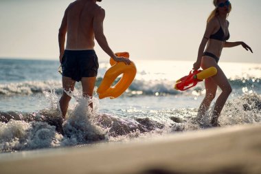 Genç bir çift güzel bir yaz gününde sahilde sığ sularda oyuncaklarla oynamaktan hoşlanır. Yaz, sahil, deniz, tatil