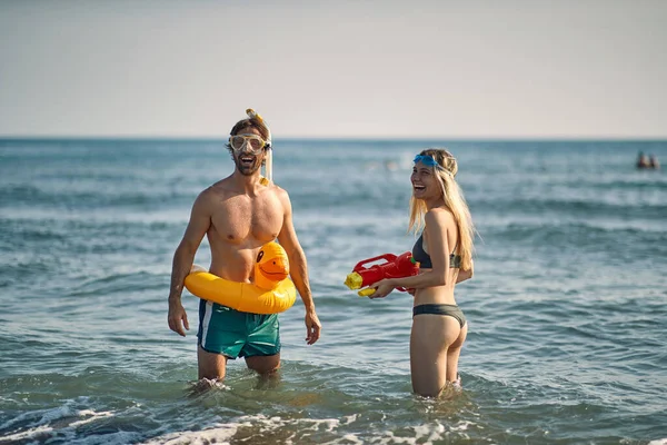 ビーチで水銃を持つルビーアヒルと笑顔の女性とクレイジー若い男 夏休みのビーチでの楽しみ — ストック写真