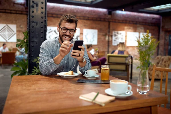 咖啡馆里快乐的年轻人微笑着看着电话 现代工业咖啡店背景 生活方式 商业概念 — 图库照片