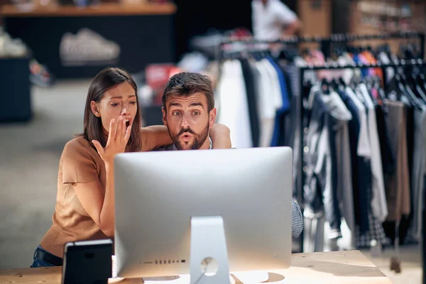 画面を見てコンピュータのデスクトップの前に若い男と女性が驚いている 統計を見る衣料品店の同僚 — ストック写真