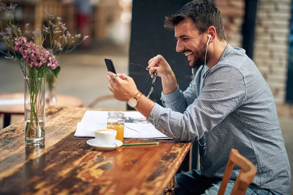 スマートフォン ビデオ通話を使用して単独で座ってハンサムな陽気な若いビジネスマン モダンなカフェインテリア — ストック写真