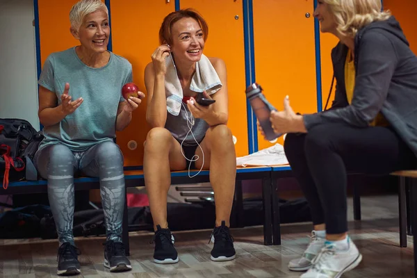 两名成熟的老年女性和穿着运动服的年轻女性在训练后坐在更衣室里 进行对话 享受在一起的时光 — 图库照片
