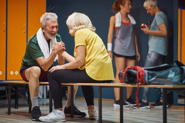 Senior man and woman arm wrestling and having fun in gym locker room. Health, wellness, active lifestyle concept.