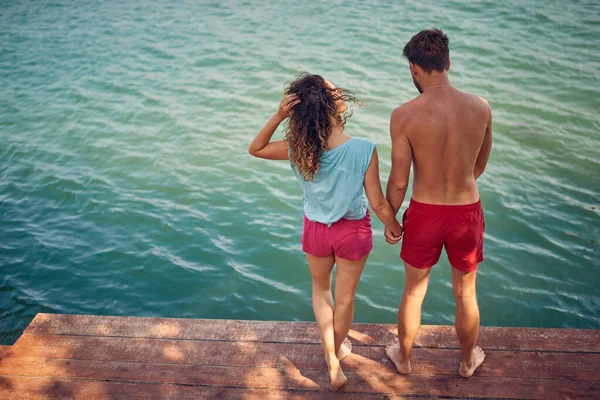 在一个美丽的夏日 一对恋爱中的年轻夫妇手牵手站在河岸的码头上 — 图库照片