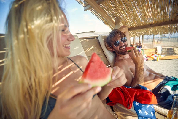 ビーチで日光浴をしながら夏を楽しむカップルはスイカを食べる — ストック写真