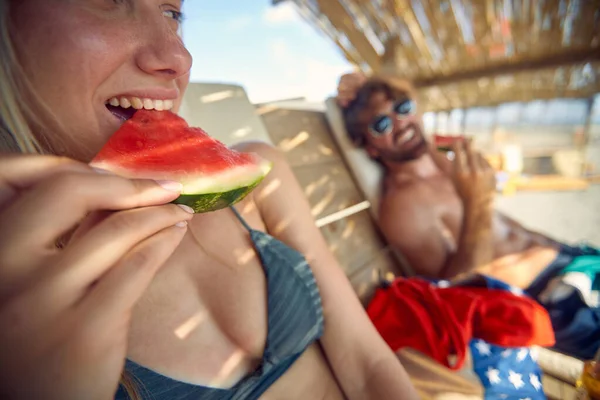 ビーチで若いカップルスイカを食べる 一緒に休暇を楽しんで男と女 レジャー ライフスタイルのコンセプト — ストック写真