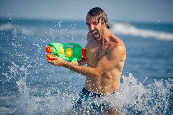 Młody Przystojny Mężczyzna Plaży Strzelający Wodą Pistoletu Wodnego Wzbudzający Emocje — Zdjęcie stockowe