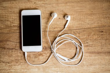 Ahşap arka planda kulaklıkları olan akıllı telefonlara yakın plan. (Üst Manzara) Müzik konseptini dinle.