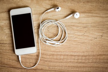 Ahşap arka planda kulaklıkları olan akıllı telefonlara yakın plan. (Üst Manzara) Müzik konseptini dinle.