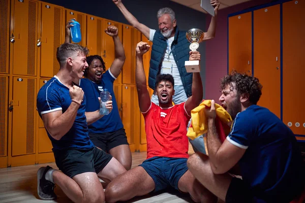 一群年轻的足球运动员在更衣室里庆祝胜利 他们的背景是他们的高级教练 积极生活方式概念 — 图库照片