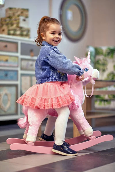 快乐快乐的蹒跚学步的小女孩坐在摇曳的独角兽上 — 图库照片