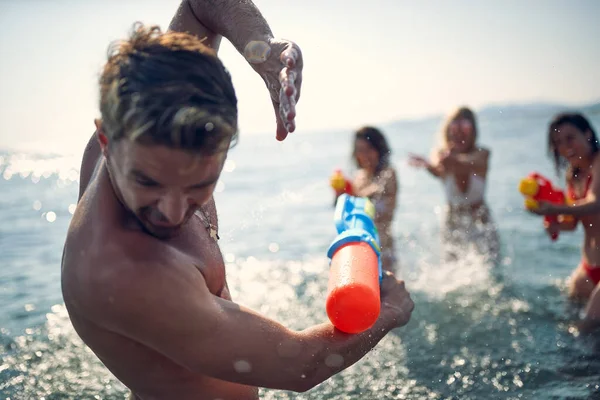 水鉄砲で男を攻撃する3人の女の子 友人の若いグループは 水の中で 海で水鉄砲で遊んでいる 一緒に 楽しい ライフスタイルの概念 — ストック写真
