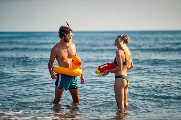 장난을 좋아하는 해변에서 오리를 남자가 구글링을 여자를 물총으로 쳐다보고 있습니다 — 스톡 사진