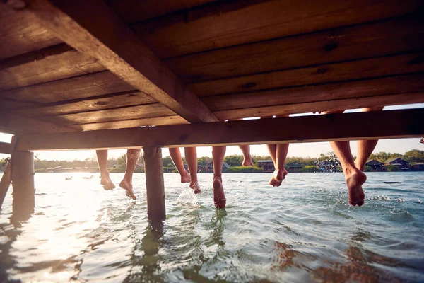 足を水にぶら下げている4人 休暇で水で友人 楽しみ 楽しさ ライフスタイルの概念 — ストック写真