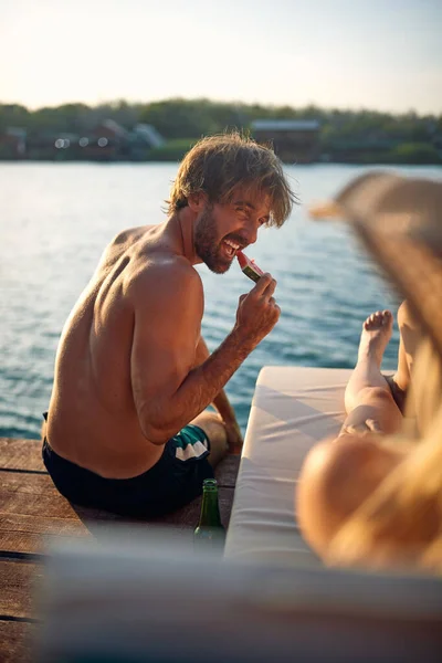 美しい夏の日に川岸で果物を食べながら太陽を楽しむ水着の若いカップルのクローズアップ — ストック写真