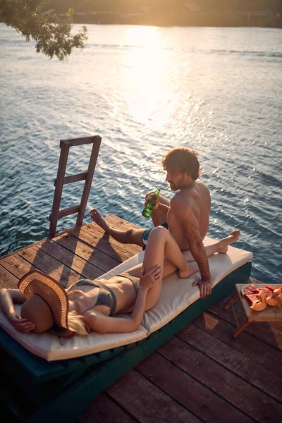 美しい夏の日に川の岸でリラックスして日光浴をしながら 水着で若いカップル — ストック写真