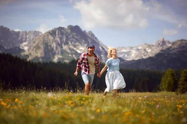 山の緑の畑を駆け抜ける幸せな男と女 夏の旅行休暇にカップルの自由を笑顔 — ストック写真