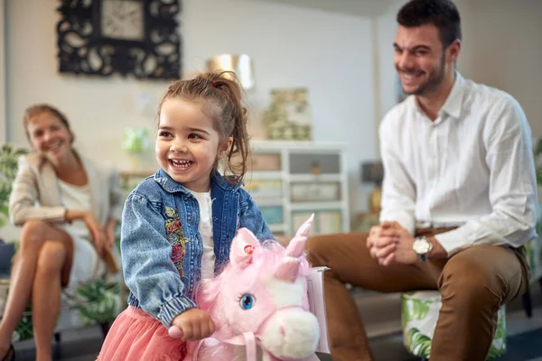 家具店でピンクのユニコーンロッキングホースに乗ってかわいい幼児の女の子 一緒に家の装飾店で素敵な家族 ショッピング ライフスタイル 家族のコンセプト — ストック写真