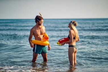 Sahilde oynaşan bir çift. Plastik ördek yüzen ve Google 'da dalış yapan bir adam su tabancası olan bir kadına bakıyor. Tatil, yaz tatili, yaşam tarzı konsepti.