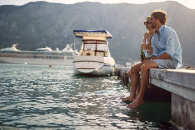 Genç bir çift sahilde rıhtımda oturuyor ve güneşli bir günde manzaranın tadını çıkarıyor. Aşk, ilişki, tatil, deniz