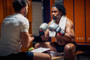 Ciddi bir boks oyuncusu soyunma odasında koçun talimatlarını alırken yüz yüze oturuyor. Antrenmana hazırlanıyorum..