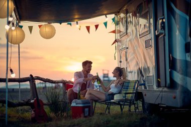 Genç bir çift tatil sırasında kampta oturuyor ve güzel bir gün batımında içiyorlar. Tatil, ilişki, kamp, doğa