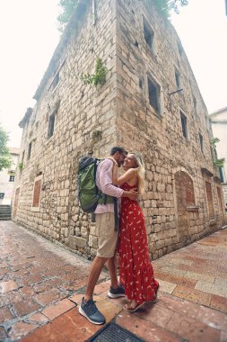 Genç aşık bir çift, deniz kenarında güzel bir günde eski şehirde yürürken kucaklaşır. Tatil, deniz kenarı, ilişki, turistler
