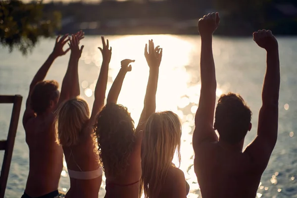 Grupa Przyjaciół Strojach Kąpielowych Cieszy Się Zachodem Słońca Nad Brzegiem — Zdjęcie stockowe