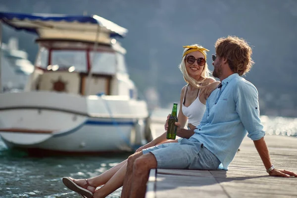 女人和男朋友调情 夫妻坐在水旁边的木制防波堤上 旅游业 生活方式概念 — 图库照片