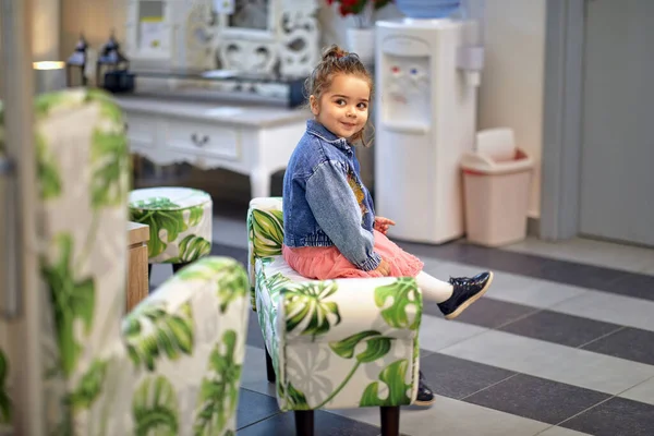 可爱的蹒跚学步的小女孩坐在一个家具店里摆满了现代家具的椅子上 环顾四周 生活方式概念 — 图库照片