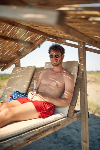 Guapo Joven Sin Camisa Tomando Sol Playa Sosteniendo Cerveza Disfrutando — Foto de Stock