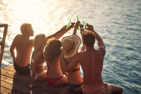 夏の晴れた日に川のほとりのドックでビールで乾杯する幸せなグループ — ストック写真