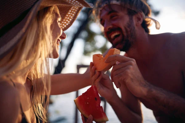 若い男と女を笑顔で休暇で一緒にスイカを食べます水の中に日没 — ストック写真