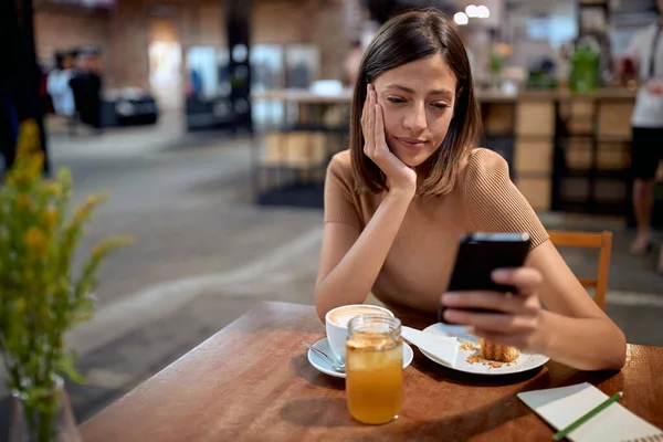Eine Junge Frau Frühstückt Café Schaut Auf Ihr Handy Und — Stockfoto