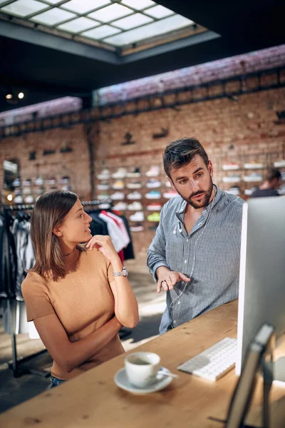 Young man and woman, employees in clothing shop talking in front of desktop computer, brainstorming, working in team on project, looking at screen. Creative ideas, business, start up concept.