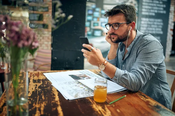Hezký Mladý Muž Brýlemi Sedí Kavárně Pomocí Chytrého Telefonu Poslouchá — Stock fotografie