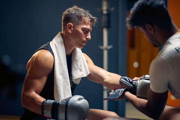 年轻的肌肉发达的拳击选手赛后在更衣室休息 教练摘下手套 生活方式概念 — 图库照片