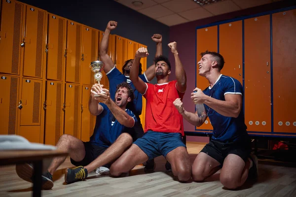 一队年轻的男足队员在更衣室里一起庆祝胜利 手握金杯 积极生活方式概念 — 图库照片