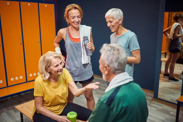 在锻炼前 与年轻女教练在体育馆更衣室里交谈的老年男女 生活方式 健康概念 — 图库照片