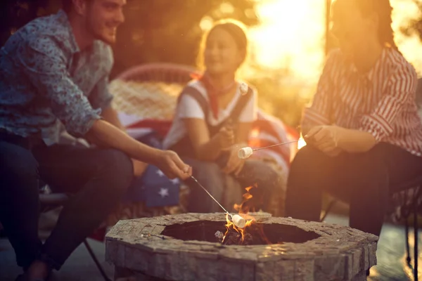 家族は独立記念日を祝うときに 激しい火の周りに集まり 喜んでマシュマロを焙煎します — ストック写真
