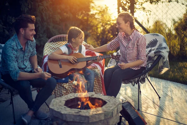 一位母亲 父亲和女儿聚集在一个舒适的火炉边 沉溺于烤棉花糖的愉快活动中 他们有才华的女儿也会弹奏古典吉他 — 图库照片