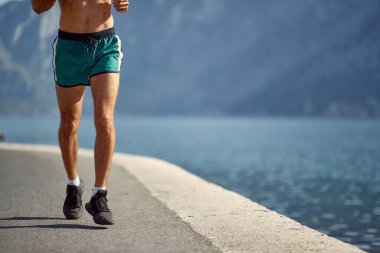 Genç yakışıklı bir adam deniz kenarında güneşli bir günde rıhtımda koşuyor. Spor, deniz, aktivite