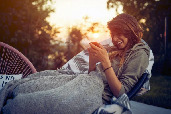 Χαρούμενη Νεαρή Γυναίκα Που Χρησιμοποιεί Smartphone Ξαπλωμένη Μια Ζεστή Καρέκλα — Φωτογραφία Αρχείου