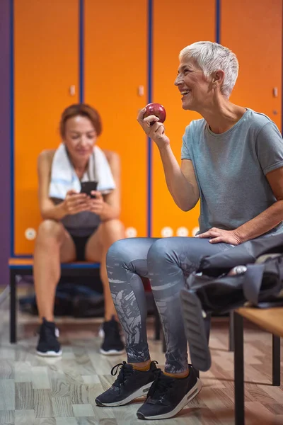 穿着运动服的老妇人坐在体育馆更衣室里 一边锻炼一边吃苹果 生活方式 福利概念 — 图库照片