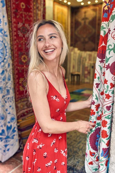 Wesoła Młoda Blondynka Przed Targiem Dywanów Tkanin Falowanej Czerwonej Sukience — Zdjęcie stockowe