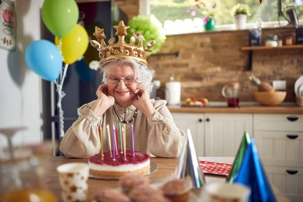 亲爱的奶奶坐在装饰精美的餐桌前 脸上挂着灿烂的笑容 照亮了整个房间 当她凝视着生日蛋糕时 眼中闪烁着欢乐的光芒 — 图库照片