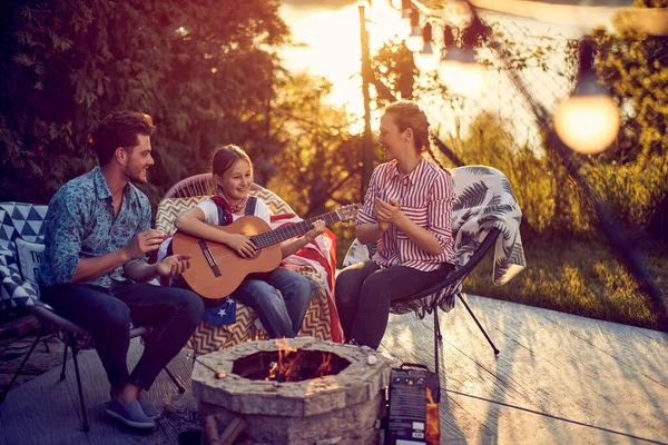 小女孩在壁炉边弹奏吉他 爸爸妈妈一边拍手一边唱 家里人在院子里享受夏日阳光的美丽景色 生活方式 家庭观念 — 图库照片