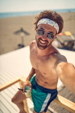 Tişörtsüz, seksi, beyaz erkek sahilde yalnız poz veriyor.