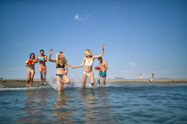 若い女の子は水鉄砲で遊ぶ夏休みの友達とビーチで楽しみを持っています — ストック写真