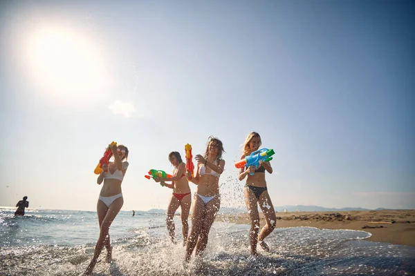 ビーチで楽しみを持っている若い友人 楽しい女の子は晴れた日にビーチで水鉄砲で楽しみを持っています — ストック写真